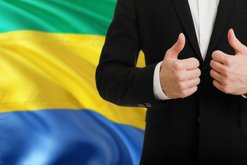 Gabon businessman showing thumbs up behind country flag with copy space. Successful international...