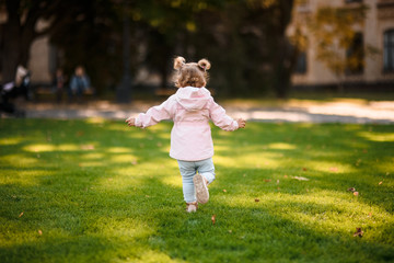 Fototapeta premium Cute little girl running in the park on the green grass