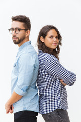 Serious pensive couple standing back-to-back, looking at camera. Young woman in casual and man in...