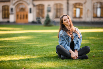 Portrait of a young woman sitting on the green grass in the autumn park