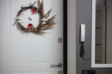 Traditional Сhristmas wreath on the front door inside with a peephole. Lifestyle. Handmade wreathe with lights and toys.  Winter holiday's decoration. 