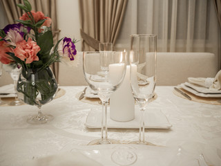Detail of table setting in beige. Elegant and romantic arrangement for dinner. Сandle, glasses and flowers.