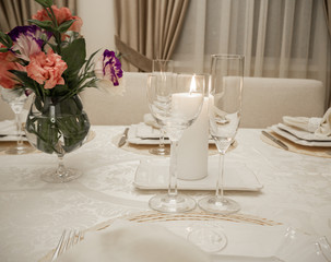 Detail of table setting in beige. Elegant and romantic arrangement for dinner. Сandle, glasses and flowers.