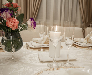 Detail of table setting in beige. Elegant and romantic arrangement for dinner. Сandle, glasses and flowers.