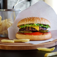 Closeup tasty burger on wooden board with beef, tomato, cheese, lettuce, fresh vegetables and french fries. Tasty hamburger cheeseburger. Fast food.