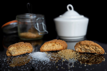 White sugar and brown sugar with three sweet cantuccini with almonds on a shiny black reflective background