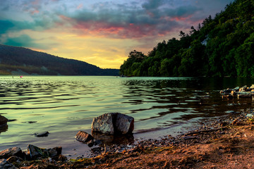 A small boulder protruding from the surface of the water as the sun sets over Devil's Lake in...