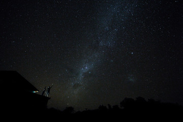 Fototapeta na wymiar Couple on rooftop watching mliky way and stars in the night sky on Bali island