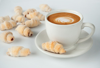 Cappuccino in white cup with heart on milk froth. A cup of coffee latte with homemade cookies bagels on a white background.