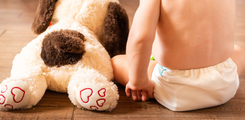 Baby wearing cloth diaper next to puppy dog stuff animal - obrazy, fototapety, plakaty