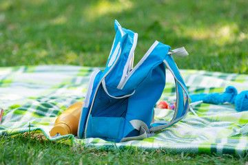 Children's backpack and bottle for water lie on a bedspread on a picnic - obrazy, fototapety, plakaty