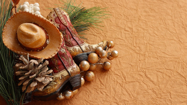 Christmas cowboy boots and hat laying with pine cones, rustic berries on a brown textured background with writing space