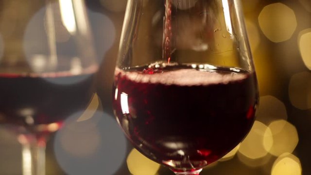 Bartender pours red wine into the glasses. Filling two glasses of red wine. Close-up of filling wine glass with red wine  against the background of bottles and New Year's flashlights.
