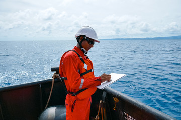 Safety officer, standing on an industrial ship, wearing overalls, a helmet, safety goggles and...