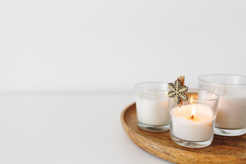 Wooden tray with white burning candles standing on white table. Cozy home decoration, interior...
