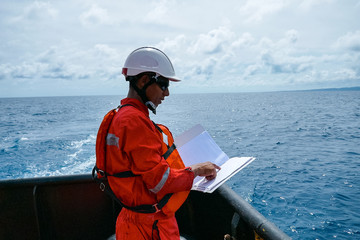Safety officer, standing on an industrial ship, wearing overalls, a helmet, safety goggles and...