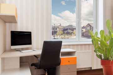 Modern work desk interior with a computer and cactus fower pot near to the window with a view of residential area spring sunny day background.