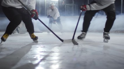 Group of male ice hockey players in helmets trying to take control of puck on rink, goaltender waiting at net - Powered by Adobe