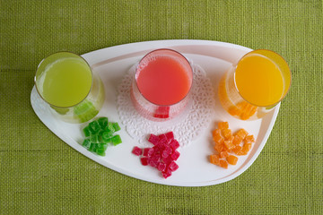 Transparent smooth glasses with colorful juice are on table. Fruits from which juice is made lie next to pieces.  Aerial view.