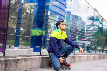 Young street Skater sitting and leaning on a wall made of glass in the street