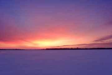 Twilight winter landscape with frozen lake and sunset sky.