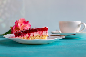 Appetizing piece of raspberry cake on plate next to cup of tea on bright blue background. Selective focus
