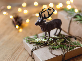 Christmas presents on shabby wooden background. Deer figure on New Year gifts in craft paper with coniferous tree branches.