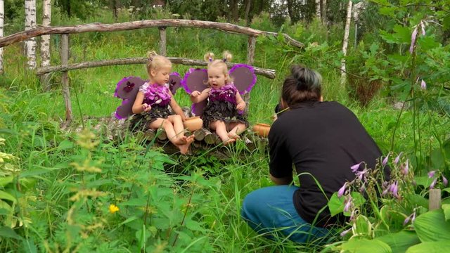 Photographer takes pictures of girls playing violet butterflies. Girls wear butterfly wings
