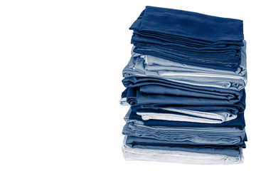 Stack of folded clean blue bedding on a white background: duvet covers, sheets, pillowcases. The concept of housework and storage. Close-up. Copy space