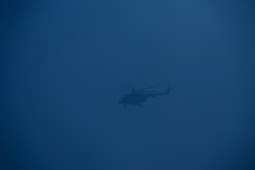 Silhouette of a helicopter flying in a trendy blue sky.