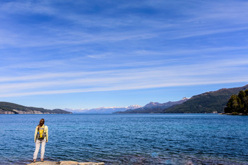 Fototapeta na wymiar Landscape view of a young woman on the Nahuel Huapi lake coast against Andes mountains in Arrayanes National Park, Villa La Angostura, Patagonia, Argentina