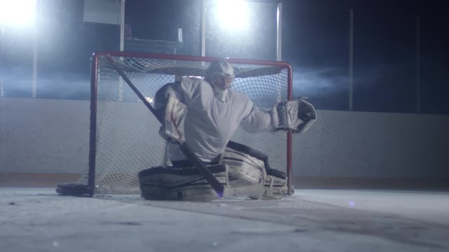 Front view of male hockey goaltender standing in the front of the net on ice rink and catching puck with glove