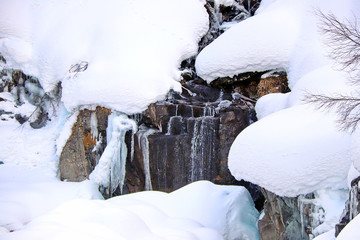 mountain stream flows among the rocks and puffy white snow on the banks