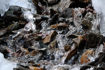 mountain stream flows trought stones, snow and ice