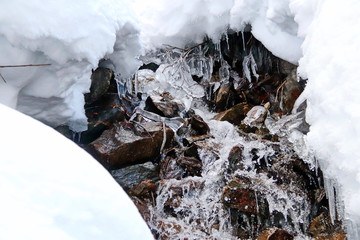 mountain stream flows trought stones, snow and ice