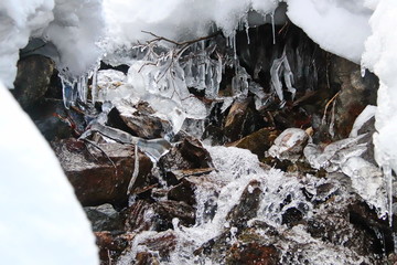 mountain stream flows trought stones, snow and ice