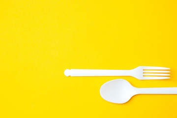 Plastic white spoon and fork on yellow background. Cooking utensil. Cutlery sign. Top view. Minimalist Style. Copy, empty space for text