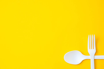 Plastic white crossed fork and spoon on on yellow background. Cooking utensil. Cutlery sign. Top view. Minimalist Style. Copy, empty space for text