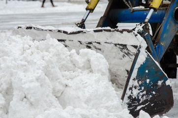City services using heavy equipment remove the streets and roads of the city from snow to prevent inevitable traffic jams. Snow and tractor bucket close-up.