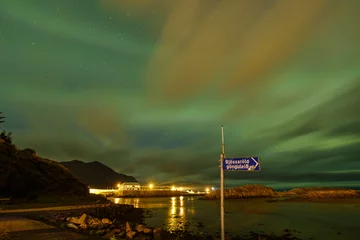 Foto op Aluminium Spectacularly beautiful green, blue and orange northern lights above a lake in Bourganes , with reflection in the water, a signpost in the foreground, Iceland © Dasya - Dasya
