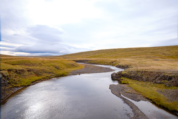 Landscape of Blondus, blue/white sky, grass, water and a flowing river in the middle in pretty autumn colours in Iceland