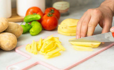 person slicing potato on cutting board for frying