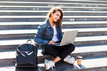 Young pretty woman sitting on the stairs with laptop on the sunny street