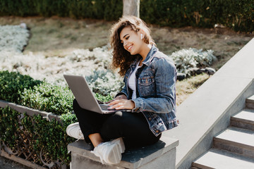 Portrait of a happy young woman sitting on the city stairs and using laptop computer outdoors