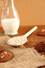 Oatmeal in a spoon, next to milk and oatmeal cookies.