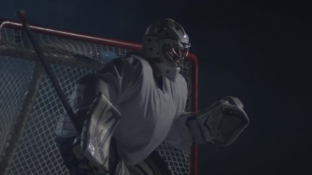 Medium shot of middle-aged male ice hockey goaltender standing in front of the net and catching puck with glove
