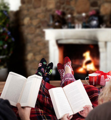 couple reading book at home, Christmas tree and gifts near fireplace