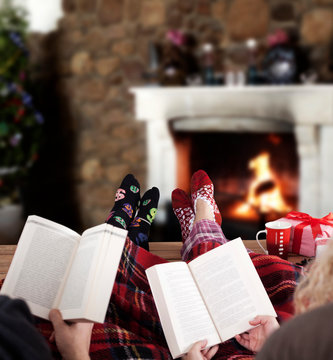 Couple Reading Book At Home, Christmas Tree And Gifts Near Fireplace