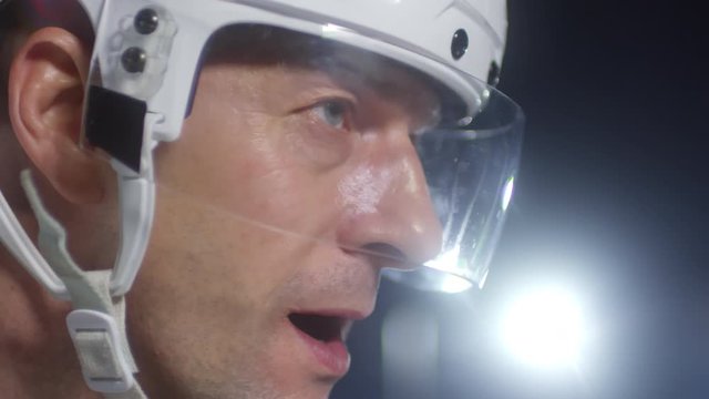 Extreme close up shot of middle-aged male ice hockey player in helmet standing on rink and waiting, then looking at camera