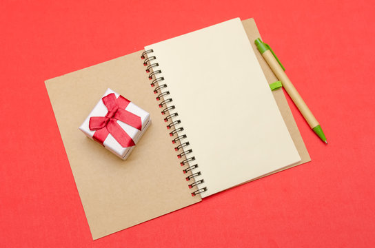 Notepad with pen and gift lies on a red background, copy space.